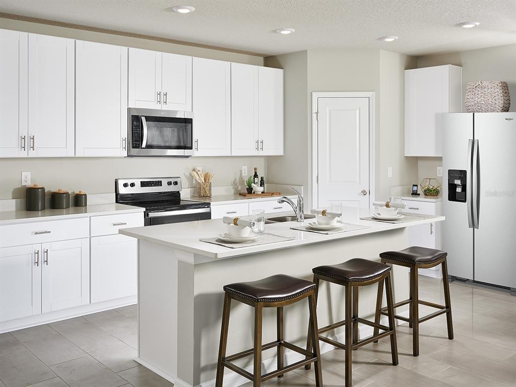 A modern kitchen features white cabinets, quartz countertops, a center island, and three bar stools — 372 CASTLE DRIVE, LAKE ALFRED, FL