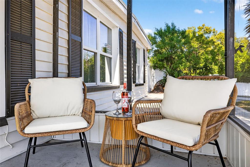 Two wicker chairs with white cushions sit on a porch beside a small round table — 9370 83RD STREET, SEMINOLE, FL