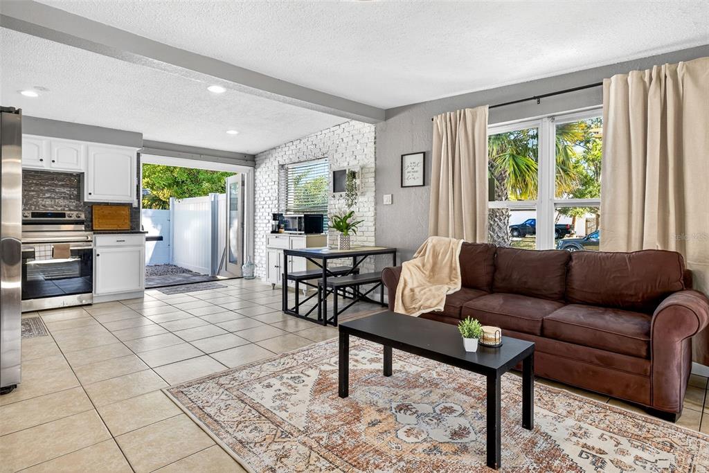 An open-concept living room and kitchen with tile floors, a brown sofa, and brick wall — 9370 83RD STREET, SEMINOLE, FL