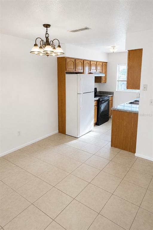 A kitchen with light tile floors, wood cabinets, a white refrigerator, and a dining chandelier — 1400 EUDORA ROAD UNIT C32, MOUNT DORA, FL