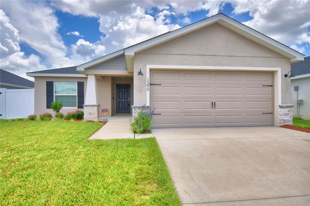 A single-story house with a beige stucco exterior, a two-car garage, and a front walkway — 1390 MEZZAVALLE WAY, AUBURNDALE, FL