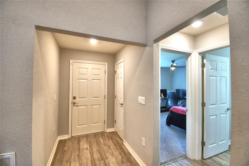 An entryway with wood-look flooring, a white front door, and a doorway leading to a bedroom — 1390 MEZZAVALLE WAY, AUBURNDALE, FL