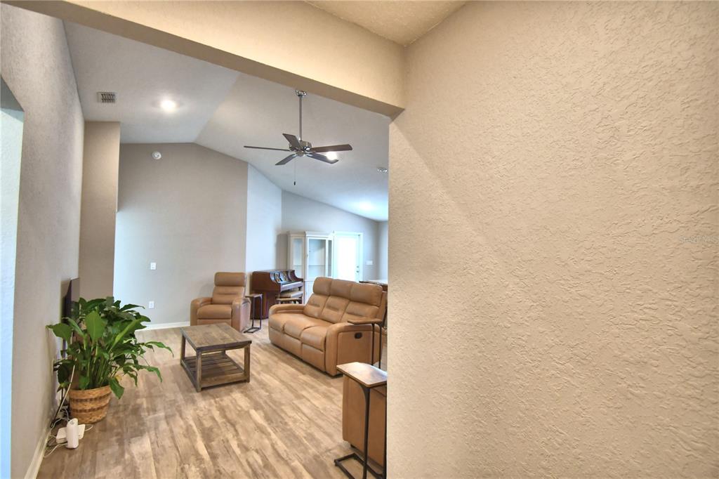 A living room with light wood-look flooring, tan leather furniture, and a vaulted ceiling — 1390 MEZZAVALLE WAY, AUBURNDALE, FL