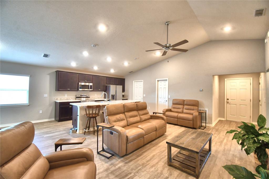 An open-concept living room and kitchen featuring brown leather furniture, wood-look flooring, and recessed lighting — 1390 MEZZAVALLE WAY, AUBURNDALE, FL