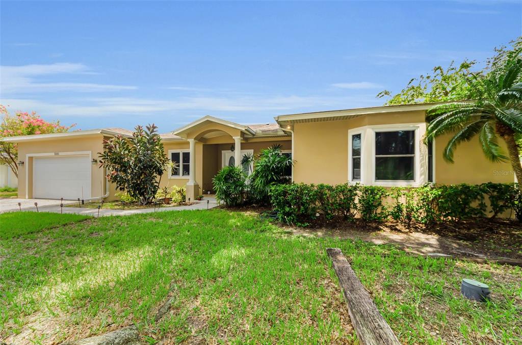 A single-story house with a two-car garage and a large tree in the front yard — 1888 BUGLE LANE, CLEARWATER, FL
