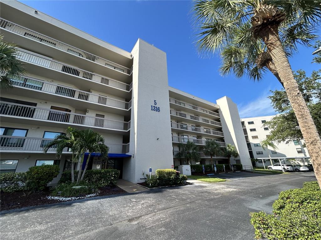 A multi-story apartment building with balconies and a parking lot under a clear blue sky — 1316 PASADENA AVENUE S UNIT 102, SOUTH PASADENA, FL