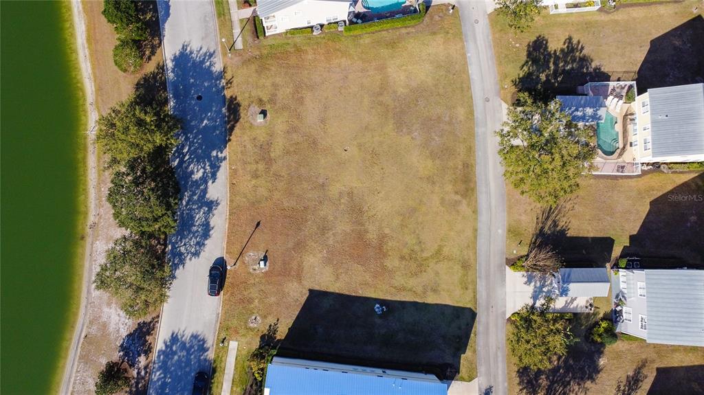 An aerial view shows a vacant residential lot situated between two paved roads and a lake — 1527 FAIRVIEW CIRCLE, REUNION, FL