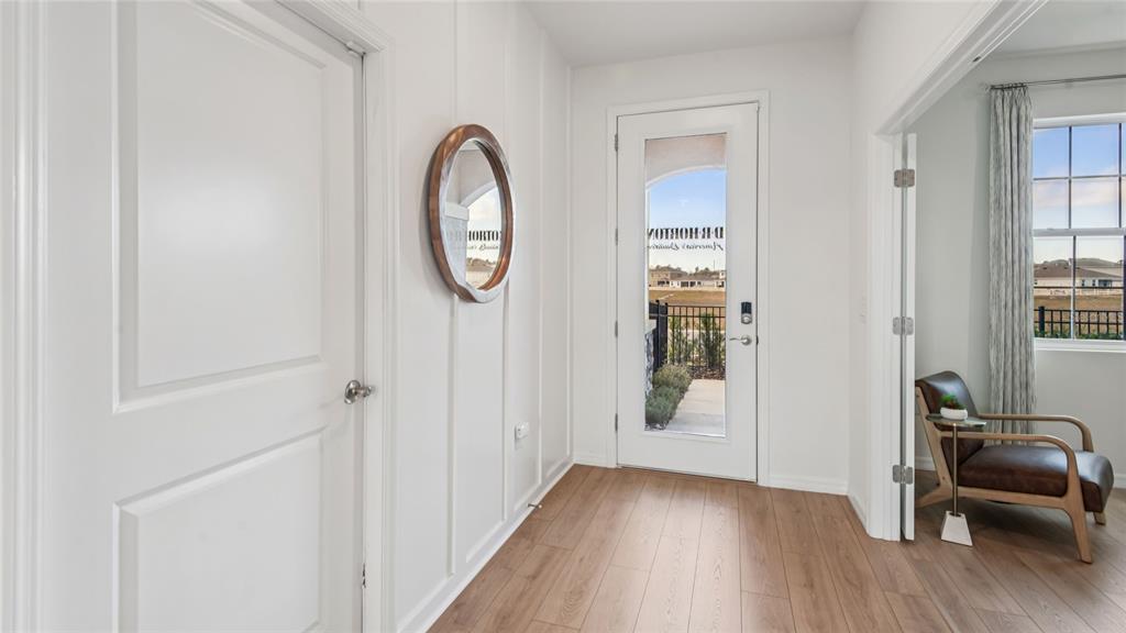 An entryway features white board-and-batten walls, wood-look flooring, a round mirror, and a glass-paneled door — 11238 DUCKLING WAY, WEEKI WACHEE, FL