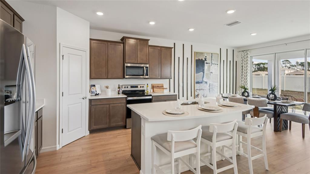 A modern kitchen features dark wood cabinets, a white island with seating, and wood flooring — 11238 DUCKLING WAY, WEEKI WACHEE, FL