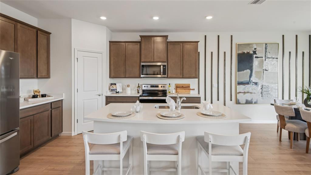 A kitchen features brown cabinets, a white island with three chairs, and light wood flooring — 11238 DUCKLING WAY, WEEKI WACHEE, FL