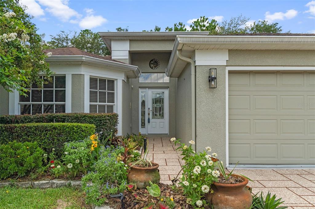 The exterior of a single-story home features a white front door, garage, and landscaped garden — 11578 NEW HAVEN DRIVE, SPRING HILL, FL