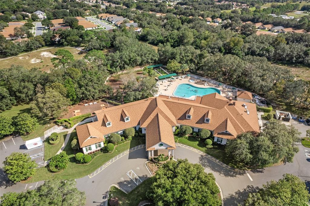 An aerial view of a community clubhouse with a swimming pool and surrounding wooded landscape — 11578 NEW HAVEN DRIVE, SPRING HILL, FL