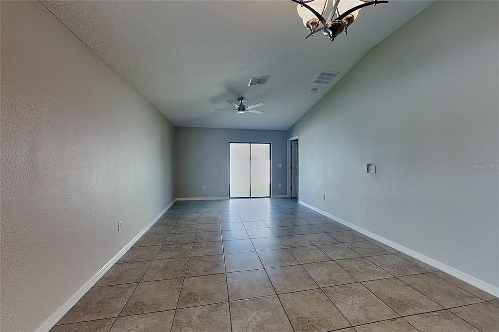 An empty room features light gray walls, tile flooring, a ceiling fan, and sliding glass doors — 10129 CARLOWAY HILLS DRIVE, WIMAUMA, FL