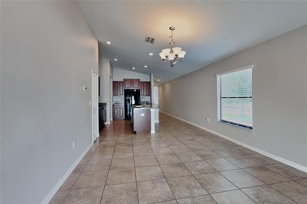 An open-concept kitchen and dining area features tile flooring, dark wood cabinets, and a chandelier — 10129 CARLOWAY HILLS DRIVE, WIMAUMA, FL