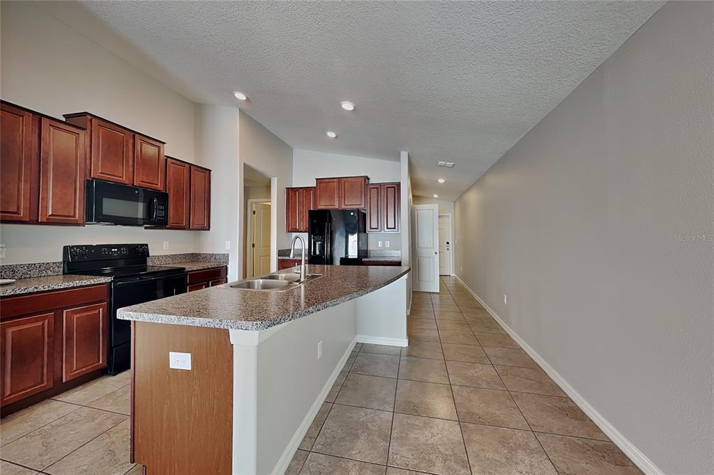 A kitchen features dark wood cabinets, granite countertops, a kitchen island, and tile flooring — 10129 CARLOWAY HILLS DRIVE, WIMAUMA, FL