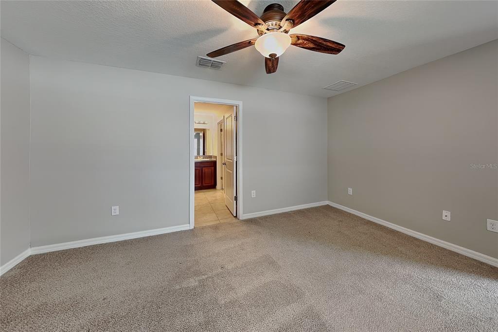A carpeted bedroom features a ceiling fan and an open doorway leading to a bathroom — 10129 CARLOWAY HILLS DRIVE, WIMAUMA, FL