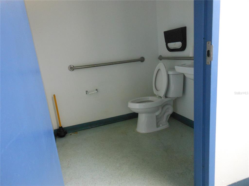 A small, accessible restroom features a white toilet, grab bars, and a plunger on the floor — 1109 SW 10TH STREET, OCALA, FL