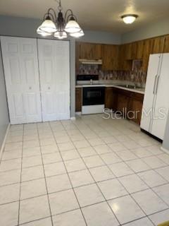 A kitchen features wood cabinets, white appliances, a tiled floor, and a dining area chandelier — 2000 SE 40TH STREET ROAD, OCALA, FL