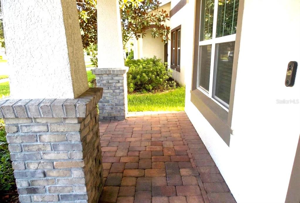 A paved walkway leads to a covered front porch with brick-accented columns and a window — 745 MARSH REED DRIVE W, WINTER GARDEN, FL