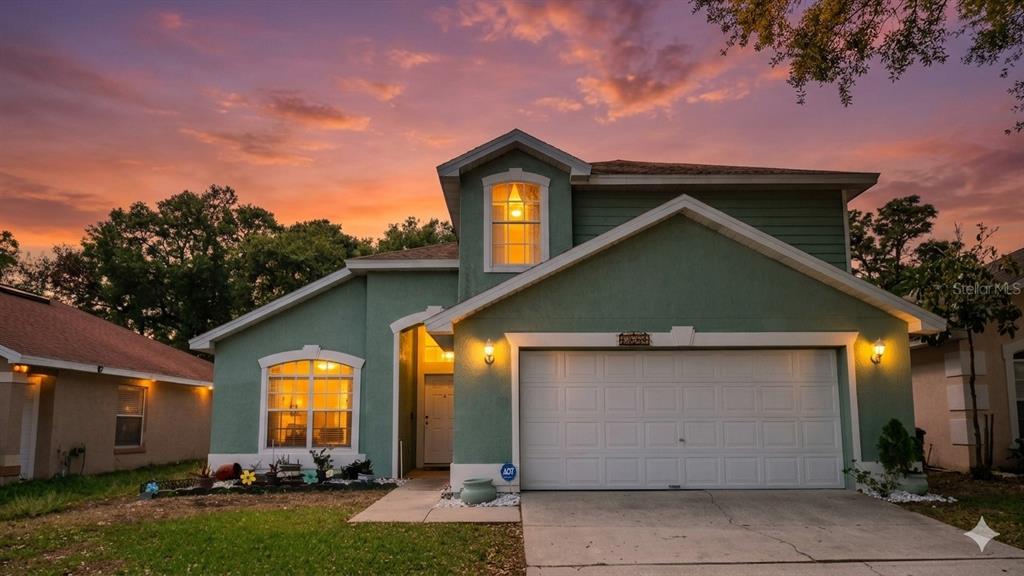 A two-story green house with a two-car garage and a sunset sky in the background — 4381 CREEKSIDE BOULEVARD, KISSIMMEE, FL