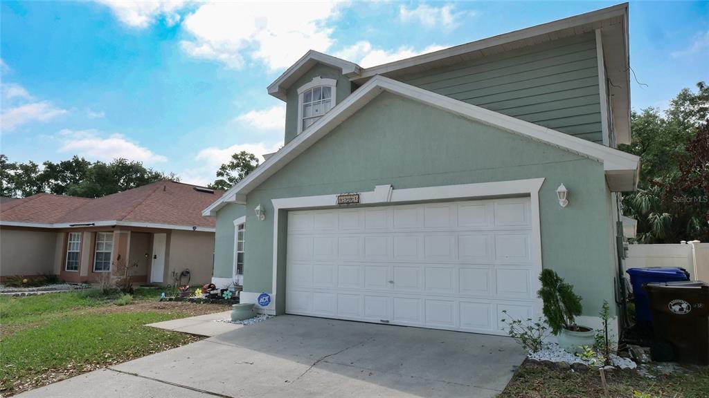 A two-story house with light green stucco and siding features a white garage door — 4381 CREEKSIDE BOULEVARD, KISSIMMEE, FL