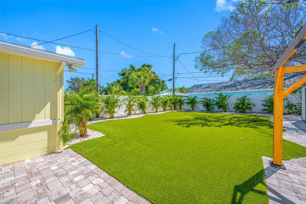 A backyard features a green turf lawn, a paver patio, and a white privacy fence — 340 79TH AVENUE, ST PETE BEACH, FL