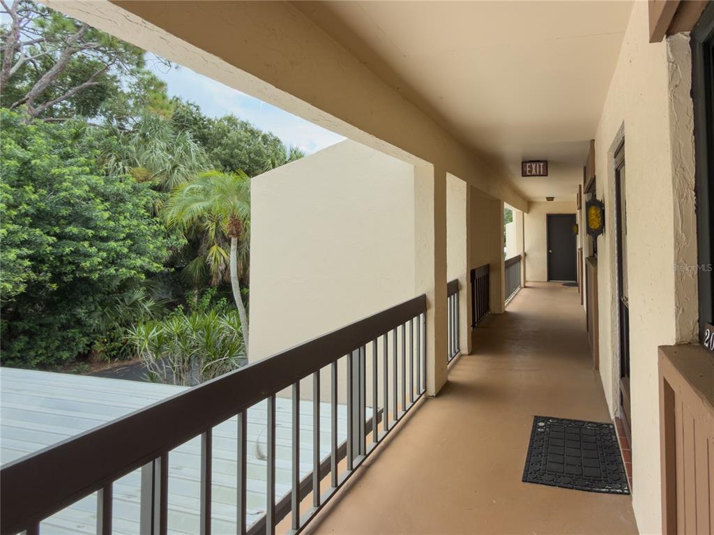 An outdoor covered walkway with a metal railing overlooks trees and a parking area — 2448 CLUBHOUSE DRIVE UNIT 202, SARASOTA, FL