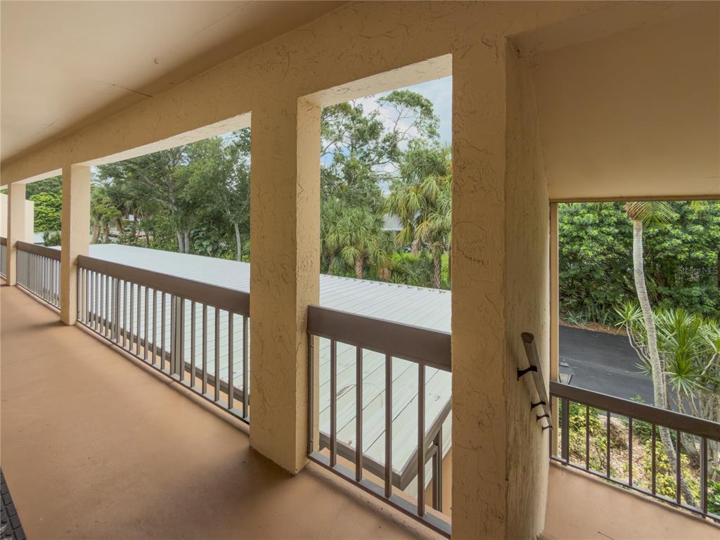 An outdoor balcony with beige stucco walls, metal railings, and views of surrounding trees — 2448 CLUBHOUSE DRIVE UNIT 202, SARASOTA, FL
