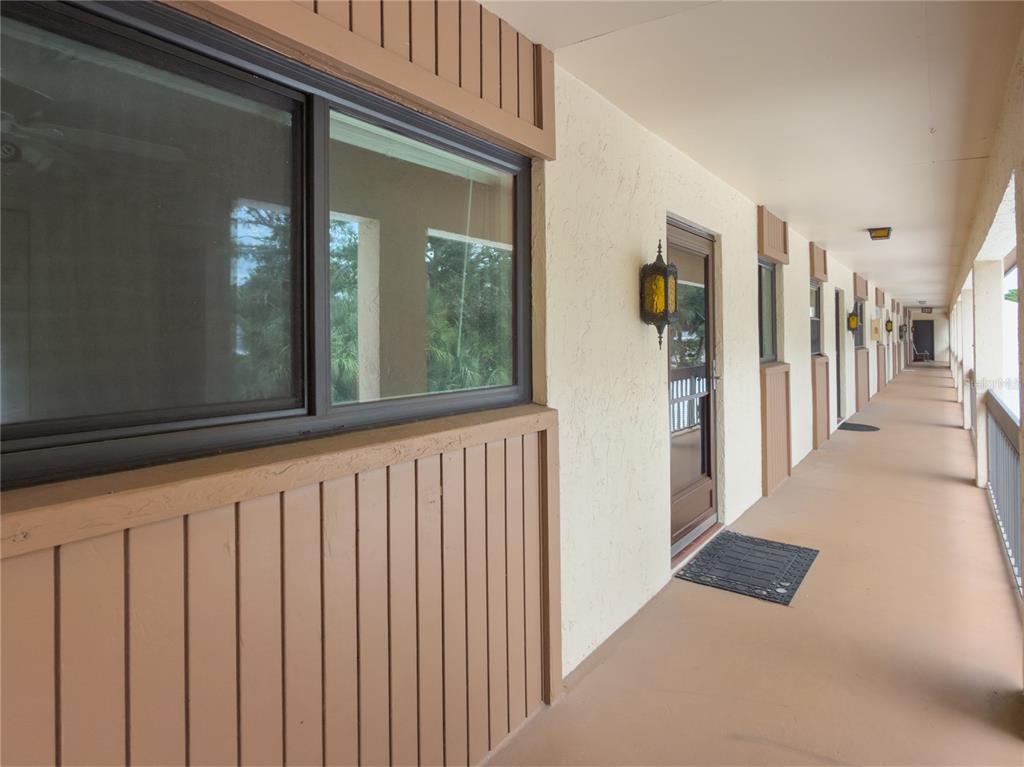An outdoor walkway with brown trim, windows, and doors along a stucco building exterior — 2448 CLUBHOUSE DRIVE UNIT 202, SARASOTA, FL