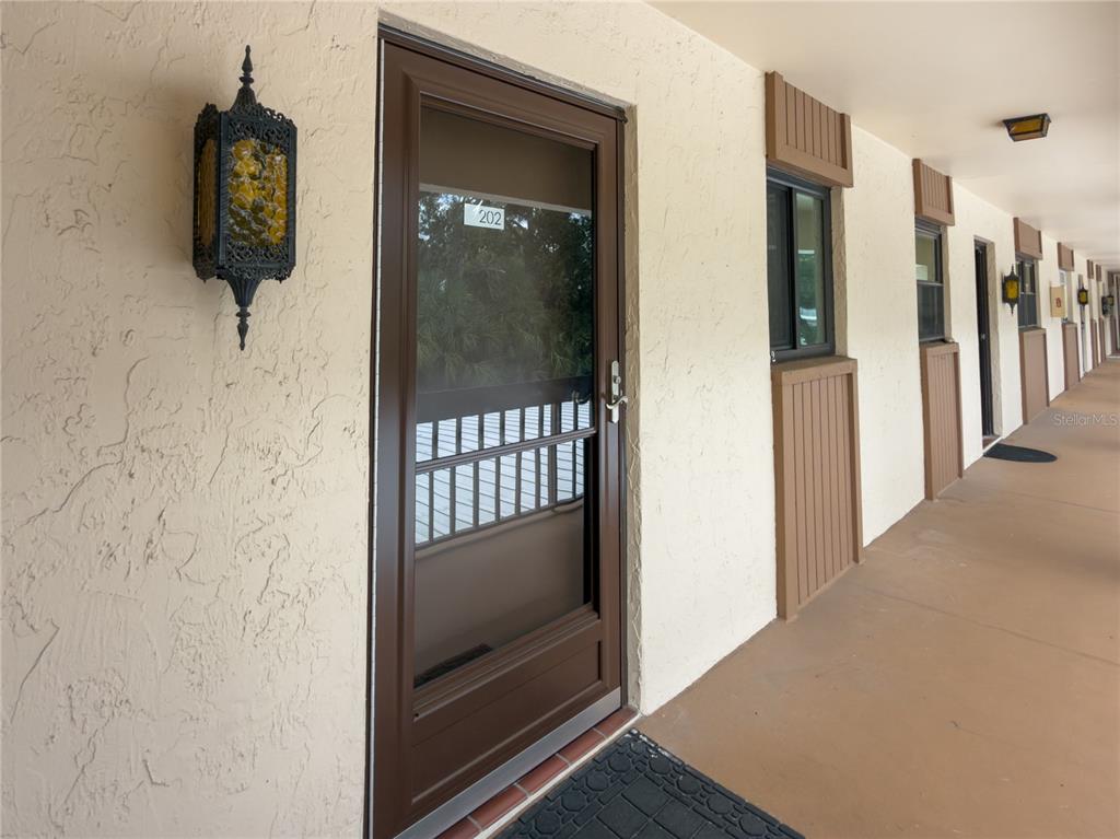 A brown storm door with the number 202 is on a beige stucco exterior walkway — 2448 CLUBHOUSE DRIVE UNIT 202, SARASOTA, FL