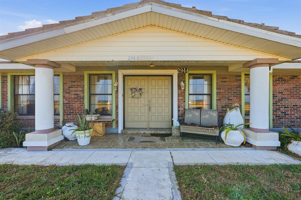 A brick house exterior features a covered porch with two white columns and double doors — 2944 OCEAN SHORE BOULEVARD, ORMOND BEACH, FL