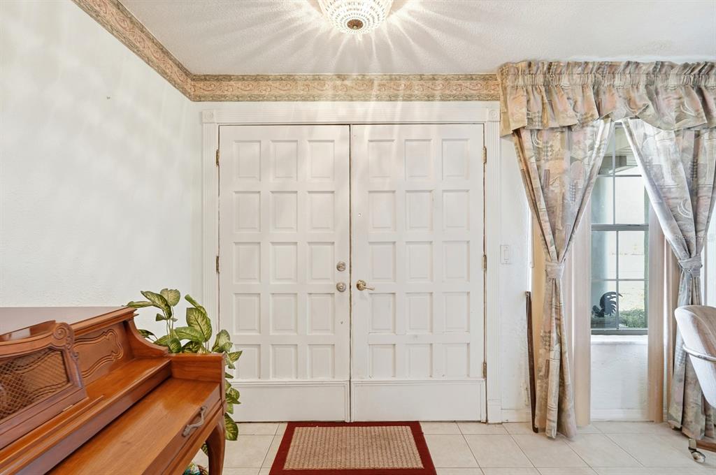 A foyer features white double doors, a wooden piano, and a window with patterned curtains — 2944 OCEAN SHORE BOULEVARD, ORMOND BEACH, FL