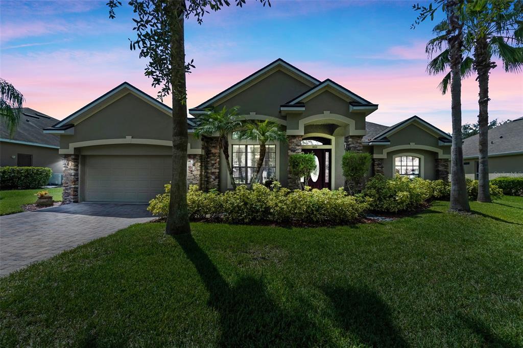 A single-story house with a two-car garage, stone accents, and palm trees at sunset — 1460 PRAIRIE OAKS DRIVE, ST CLOUD, FL