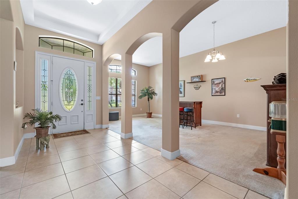 A tiled entryway leads into a carpeted living area with arched columns and a home bar — 1460 PRAIRIE OAKS DRIVE, ST CLOUD, FL