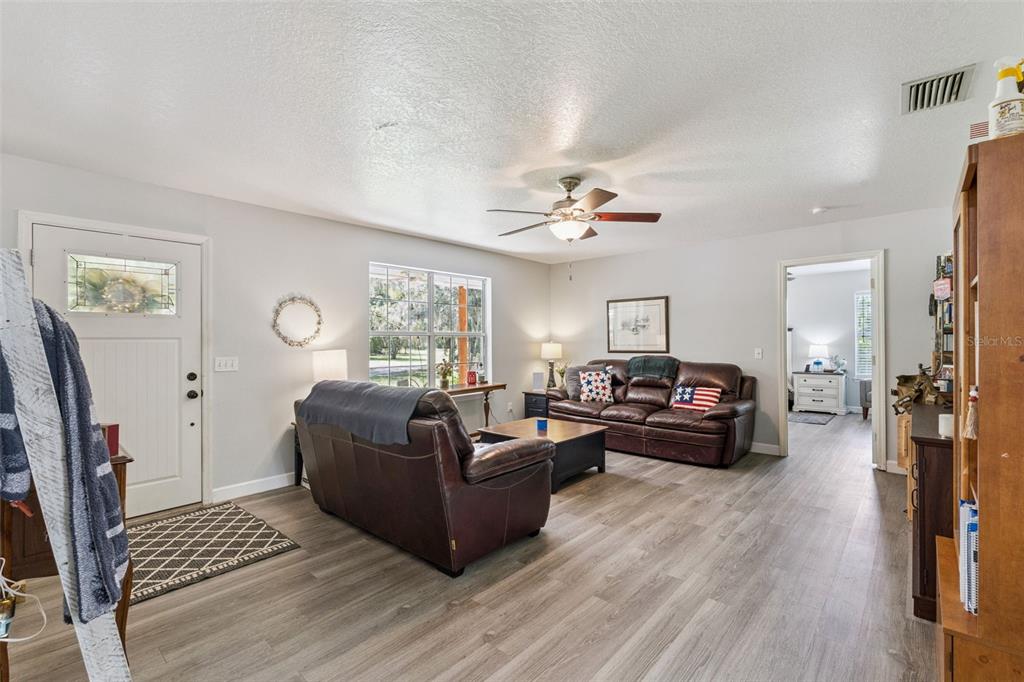 A living room features a leather sofa, a television on a fireplace console, and wood-look flooring — 5500 VENTURA ACRES ROAD, GROVELAND, FL