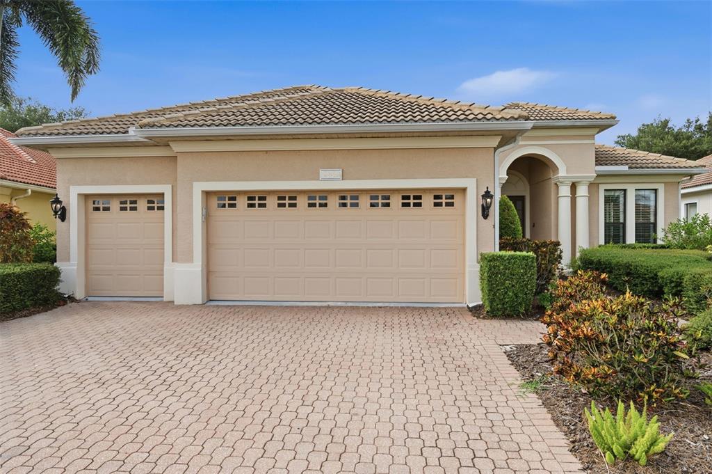 A beige single-story house with a three-car garage and a paved driveway — 13860 SIENA LOOP, BRADENTON, FL