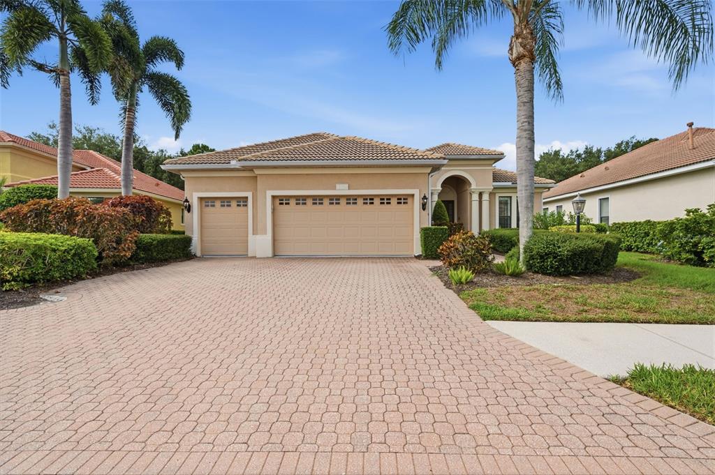 A tan single-story house with a three-car garage and a paved driveway — 13860 SIENA LOOP, BRADENTON, FL