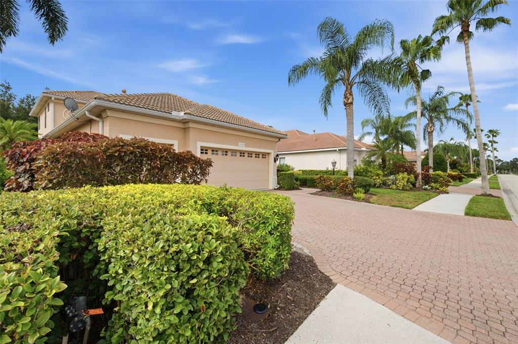 A beige house with a tiled roof and a paved driveway surrounded by lush landscaping — 13860 SIENA LOOP, BRADENTON, FL