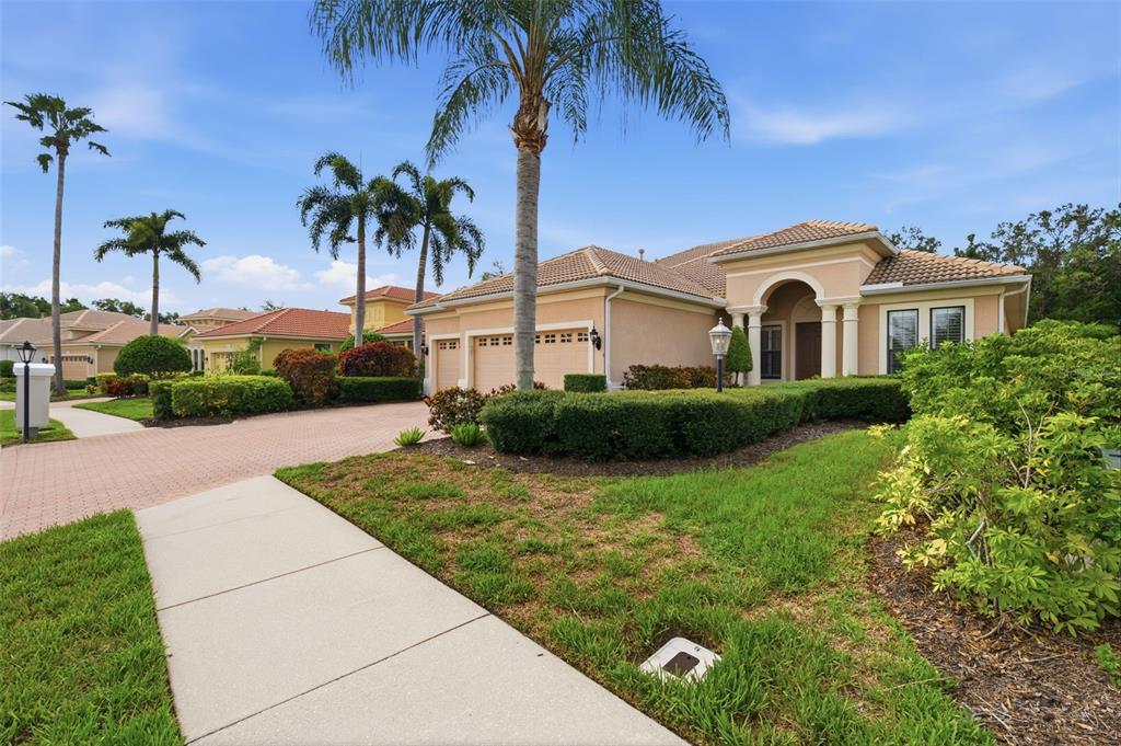 A single-story stucco house with a tile roof, three-car garage, and palm trees — 13860 SIENA LOOP, BRADENTON, FL