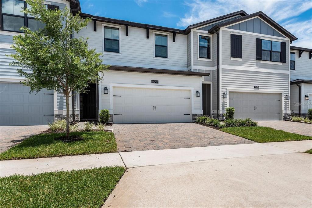 A two-story townhouse exterior features a light-colored facade, a two-car garage, and a paved driveway — 11043 WHISTLING PINE WAY, ORLANDO, FL