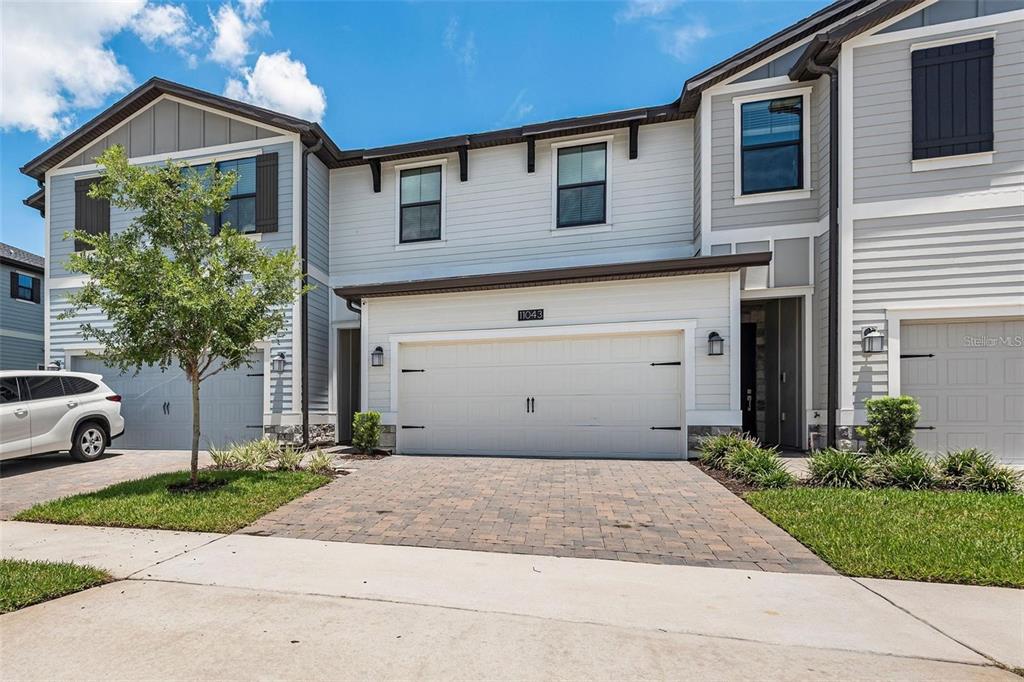 A two-story townhouse exterior features a paved driveway, a white garage door, and light-colored siding — 11043 WHISTLING PINE WAY, ORLANDO, FL