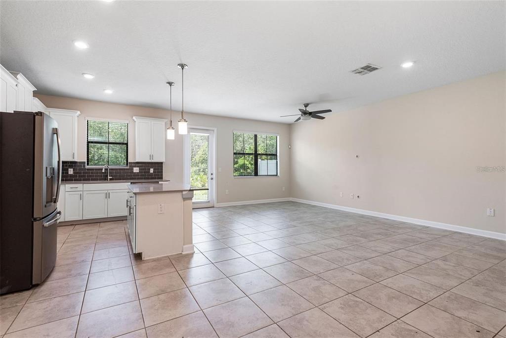 An open-concept kitchen and living area features tile flooring, white cabinetry, and a ceiling fan — 11043 WHISTLING PINE WAY, ORLANDO, FL