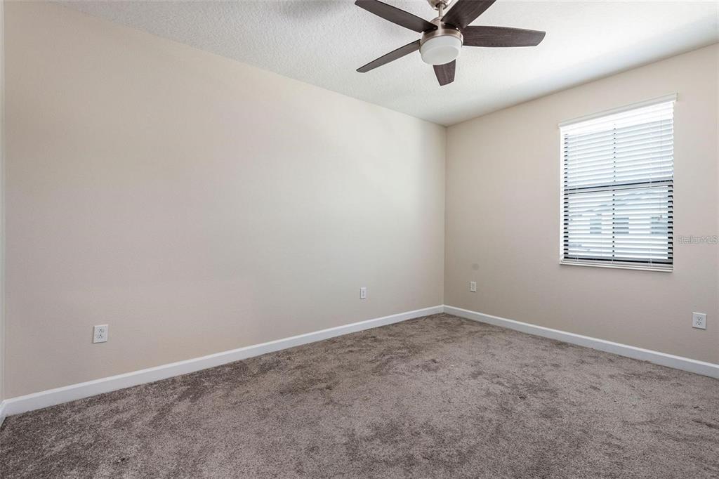 An empty bedroom features beige walls, gray carpeting, a ceiling fan, and a window with blinds — 11043 WHISTLING PINE WAY, ORLANDO, FL