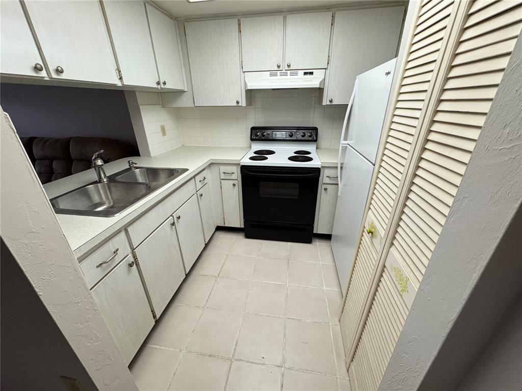 A kitchen features white cabinets, a black stove, a white refrigerator, and tiled flooring — 1250 S PINELLAS AVENUE UNIT 511, TARPON SPRINGS, FL