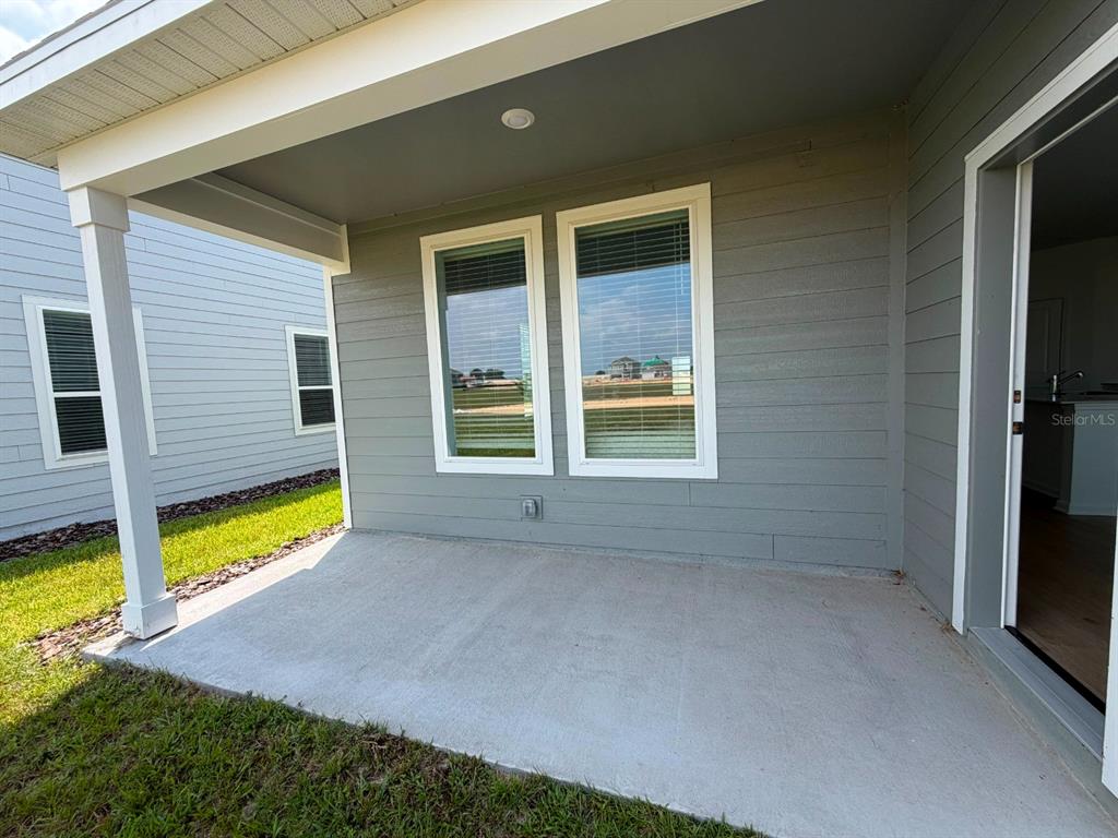 A covered concrete patio features gray horizontal siding and two windows on the exterior wall — 6020 WELLBEING WAY, CLERMONT, FL