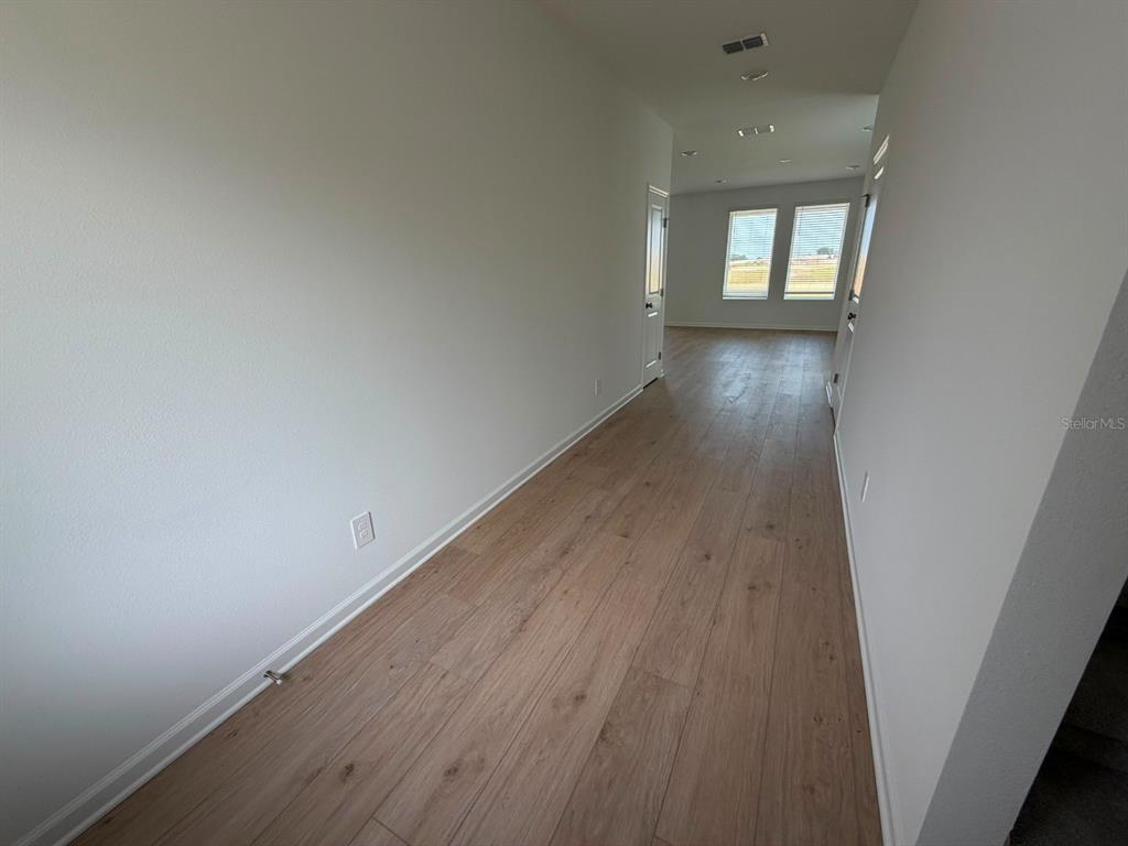 A long hallway with light wood-look flooring leads toward a room with two windows — 6020 WELLBEING WAY, CLERMONT, FL