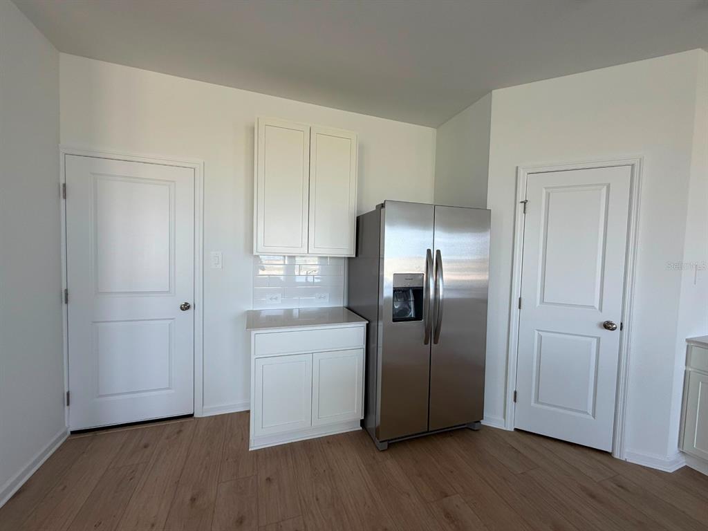 A kitchen area features white cabinets, a stainless steel refrigerator, and light wood-look flooring — 6020 WELLBEING WAY, CLERMONT, FL