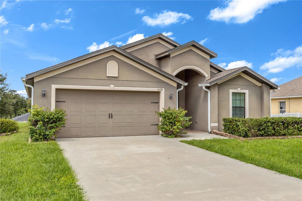 A single-story house with a beige stucco exterior, a two-car garage, and a concrete driveway — 1528 E FALMOUTH AVENUE, DELTONA, FL