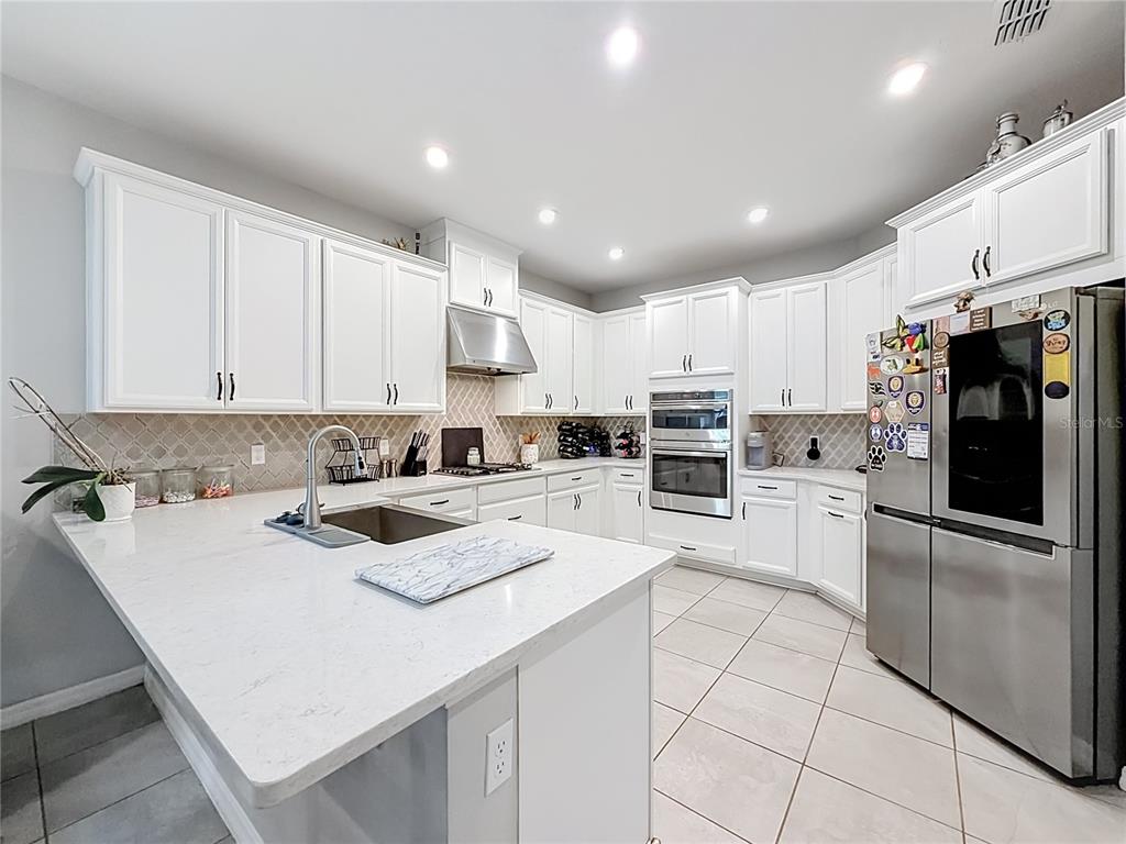 A bright kitchen features white cabinets, stainless steel appliances, and a large quartz-topped island — 2599 RIDGETOP LN, CLERMONT, FL