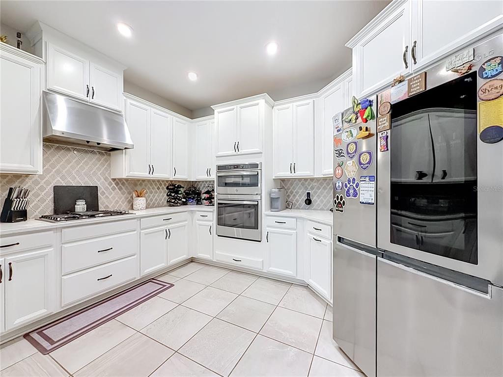 A white kitchen features stainless steel appliances, tile flooring, and a patterned backsplash — 2599 RIDGETOP LN, CLERMONT, FL